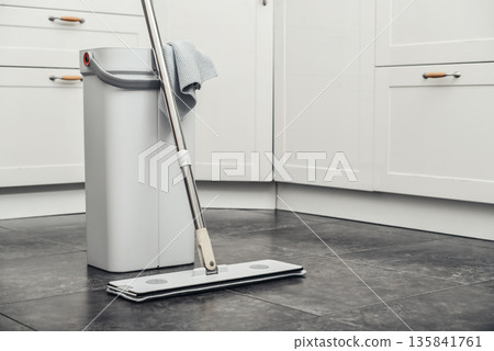 Cleaning supplies: mop, bucket with wringer sitting on tile floor in modern kitchen Cleaning supplies: mop, bucket with wringer sitting on tile floor in modern kitchen 135841761