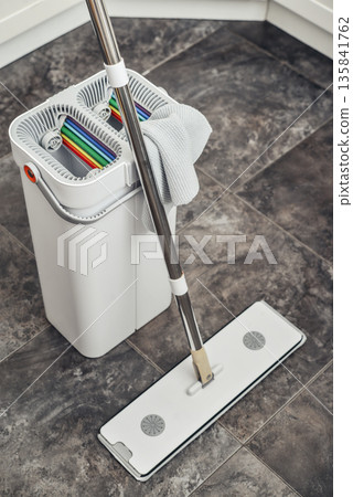 Cleaning supplies: mop, bucket with wringer sitting on tile floor in modern kitchen Cleaning supplies: mop, bucket with wringer sitting on tile floor in modern kitchen 135841762