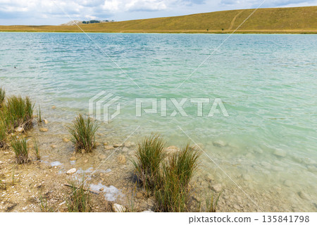 A tranquil turquoise lake lapping a rocky, pebbled shore 135841798