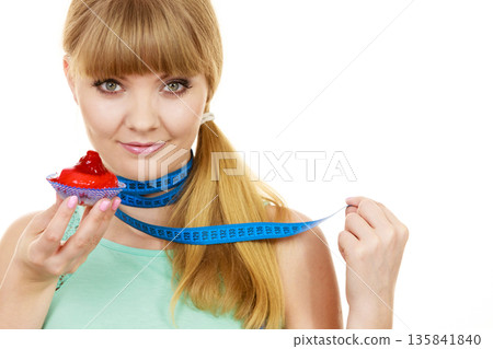Woman holds cupcake and measuring tape. Diet 135841840