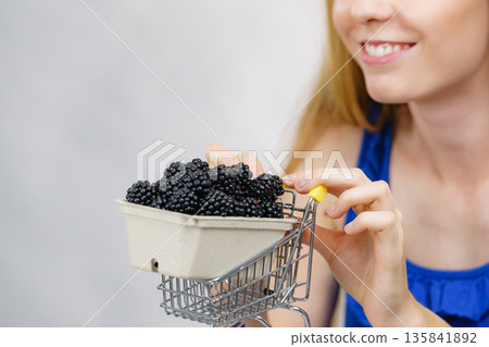 Girl holds blackberry fruits in shopping cart 135841892