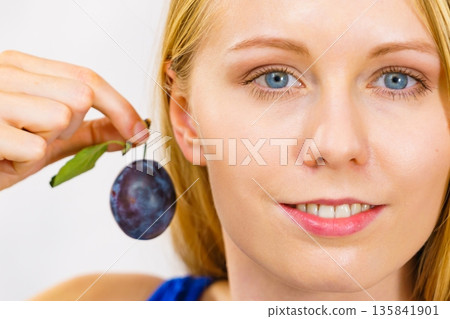Girl holds plum fruit to her ear 135841901