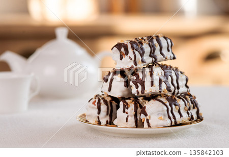 Stack of chocolate-drizzled meringue cookies with nuts on a white plate, tea time setting. Stack of chocolate-drizzled meringue cookies with nuts on a white plate, tea time setting. 135842103