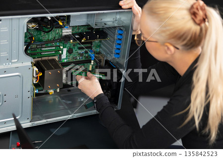 Female IT technician in her 30s installs a PCIe card inside a server motherboard during maintenance 135842523