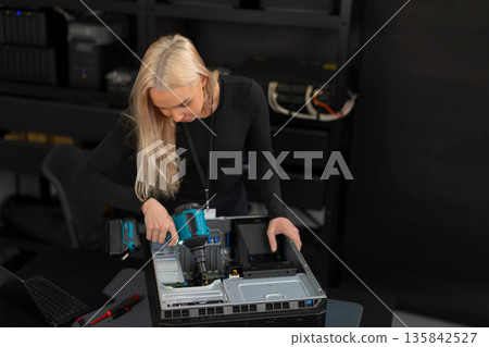 Female IT technician in her 30s repairs a server inside a computer lab with tools 135842527