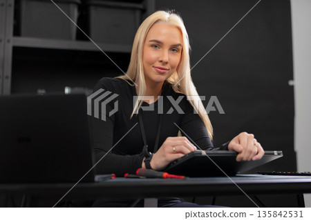 Caucasian woman IT technician in a modern office, working on a laptop and tablet at the desk 135842531