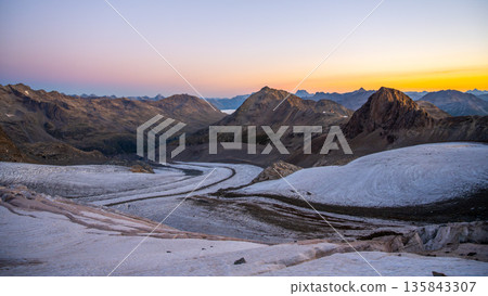 Early morning light illuminates Pers Glacier in the Bernina Range, showcasing the majestic Swiss Alps. The serene landscape features winding glacial terrain and rugged mountain peaks. 135843307