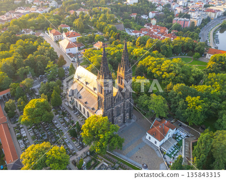 Morning light illuminates Vysehrad Basilica of St. Peter and St. Paul in Prague, showcasing its stunning architecture surrounded by lush greenery and the charm of the historic area. 135843315
