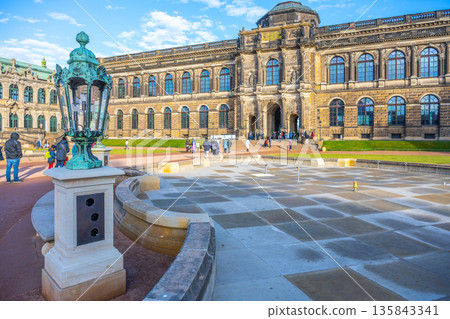 People walk around the Zwinger complex in Dresden, Germany. The beautiful architecture reflects Baroque style. The atmosphere is festive with holiday decorations present. People walk around the Zwinger complex in Dresden, Germany. The beautiful architecture reflects Baroque style. The atmosphere is festive with holiday decorations present. 135843341