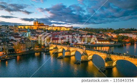Prague Castle and Charles Bridge are illuminated at night. This aerial view shows the Vltava River and the city of Prague during evening hours. The lights reflect on the water. Prague Castle and Charles Bridge are illuminated at night. This aerial view shows the Vltava River and the city of Prague during evening hours. The lights reflect on the water. 135843354