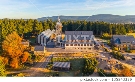 Kralovka Lookout Tower stands proudly in the Jizera Mountains. Surrounded by vibrant autumn foliage, visitors enjoy the scenic beauty of nature's fall colors and clear skies. 135843359