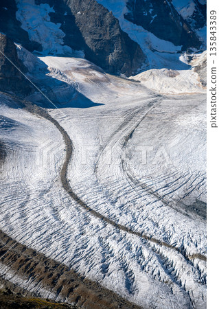 The dramatic Pers Glacier stretches across the Bernina Range, showcasing its vast icy surface and rugged alpine surroundings under clear skies in Switzerland. The dramatic Pers Glacier stretches across the Bernina Range, showcasing its vast icy surface and rugged alpine surroundings under clear skies in Switzerland. 135843389