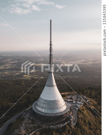 Jested Mountain Hotel stands proudly against the evening sky, showcasing its unique design. The sunset casts a warm glow over the hotel and surrounding views near Liberec. 135843395