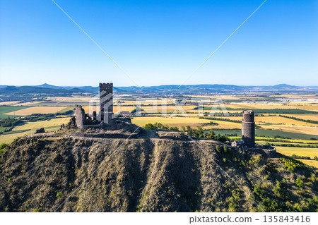 Hazmburk castle ruins rise dramatically atop a hill in Czechia, surrounded by the scenic Central Bohemian Uplands. The historical site offers breathtaking views of the lush, expansive landscape below. Hazmburk castle ruins rise dramatically atop a hill in Czechia, surrounded by the scenic Central Bohemian Uplands. The historical site offers breathtaking views of the lush, expansive landscape below. 135843416