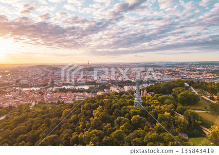 The Petrin Lookout Tower stands majestically at sunrise, surrounded by lush greenery and overlooking the stunning city of Prague, with its historic architecture bathed in golden light. The Petrin Lookout Tower stands majestically at sunrise, surrounded by lush greenery and overlooking the stunning city of Prague, with its historic architecture bathed in golden light. 135843419