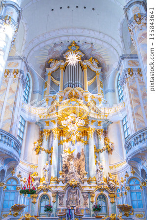 The interior of Frauenkirche in Dresden features a large dome, detailed decorations, and a grand altar. Visitors admire the artwork and architecture in this historic church. 135843641