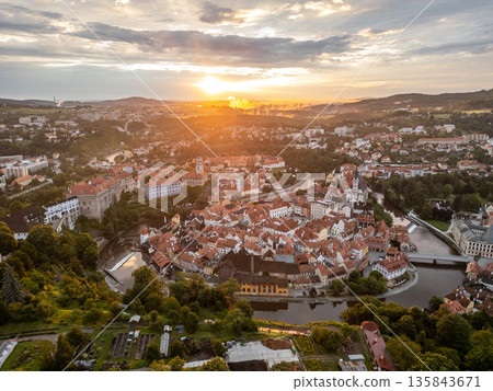 Early morning light bathes the charming town of Cesky Krumlov in a golden hue. The sun rises above the Vltava River, highlighting the UNESCO World Heritage site's stunning architecture. 135843671