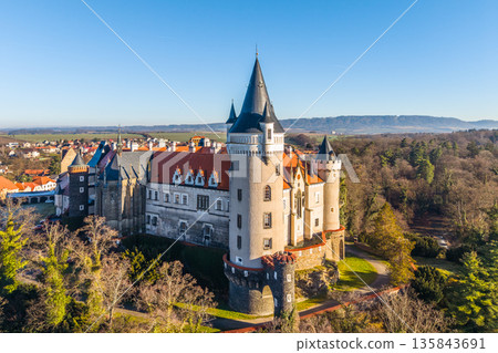An aerial view of Zleby Castle showcases its unique architecture and surrounding landscape. Green trees and distant hills frame the historic structure under a blue sky. 135843691