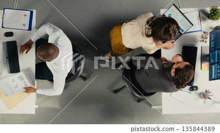 Top down view of professional employees working together in office. Diverse work team collaborates on project planning, analytics and report writing for corporate development. Top down view of professional employees working together in office. Diverse work team collaborates on project planning, analytics and report writing for corporate development. 135844389