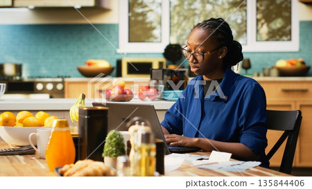 African American partners organizing financial paperwork and tax receipts at home. Checking numbers for home finances and accounting on a laptop, reflecting responsible financial habits. 135844406