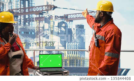 Isolated screen laptop used by drilling rig crew colleagues holding radio device to monitor systems. Engineering team on offshore platform deck using walkie talkie and chroma key notebook Isolated screen laptop used by drilling rig crew colleagues holding radio device to monitor systems. Engineering team on offshore platform deck using walkie talkie and chroma key notebook 135844408