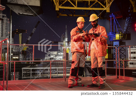Team of engineers inspecting drilling rig activity at night, ensuring efficient oil and natural fuel extraction from offshore platform. Working together on oil production for the industry. 135844432