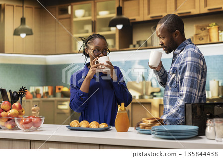Black boyfriend and girlfriend chatting over fresh coffee in the kitchen, preparing croissants and toast. Happy weekend morning filled with love and healthy homemade breakfast, lifestyle. Black boyfriend and girlfriend chatting over fresh coffee in the kitchen, preparing croissants and toast. Happy weekend morning filled with love and healthy homemade breakfast, lifestyle. 135844438
