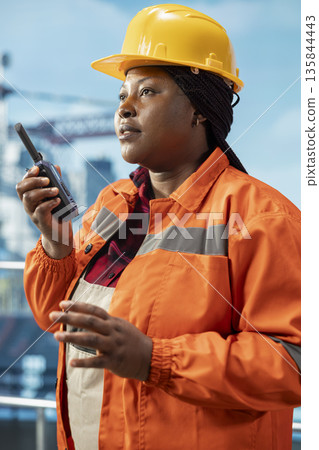 Closeup of oil company manager on drilling barge using walkie talkie to ensure uninterrupted communication with onsite workers. Woman on offshore platform transmits instructions through radio device Closeup of oil company manager on drilling barge using walkie talkie to ensure uninterrupted communication with onsite workers. Woman on offshore platform transmits instructions through radio device 135844443