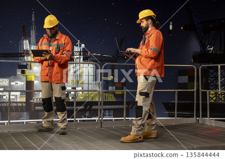 Drilling barge engineer managing operational workflows using tablet app during night shift. Offshore platform employee documenting hazard reports and safety inspections on device Drilling barge engineer managing operational workflows using tablet app during night shift. Offshore platform employee documenting hazard reports and safety inspections on device 135844444