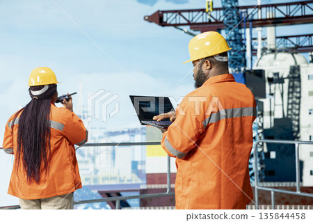 Offshore platform specialists using artificial intelligence tech on device to optimize drilling operations. Employees using notebook, monitoring barge activity using AI technology Offshore platform specialists using artificial intelligence tech on device to optimize drilling operations. Employees using notebook, monitoring barge activity using AI technology 135844458