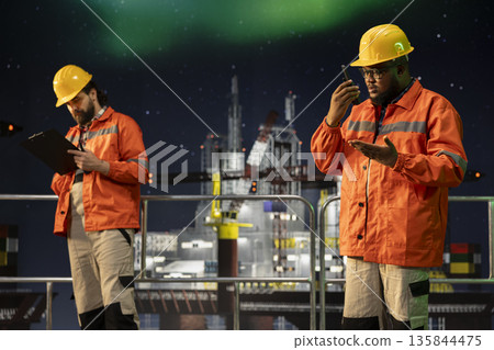 Drilling ship employee coordinating remote team tasks using portable radio system. Expert speaking into walkie talkie microphone, managing logistics on offshore sea platform Drilling ship employee coordinating remote team tasks using portable radio system. Expert speaking into walkie talkie microphone, managing logistics on offshore sea platform 135844475