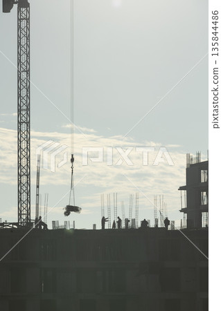 Construction company personnel building high rise condominium for new residential district project during sunny day. Ironworkers constructing concrete skyscraper structures during city expansion Construction company personnel building high rise condominium for new residential district project during sunny day. Ironworkers constructing concrete skyscraper structures during city expansion 135844486