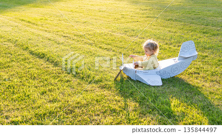 Cardboard airplane. Child pilot play outdoor. Toddler costume girl field yellow. Cardboard airplane. Child pilot play outdoor. Toddler costume girl field yellow. 135844497
