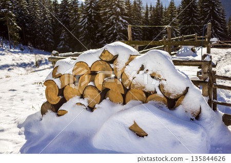 Neatly piled stack of chopped dry trunks wood covered with snow outdoors on bright cold winter sunny day, abstract background, Fire wood logs prepared for winter, ready for burning. Neatly piled stack of chopped dry trunks wood covered with snow outdoors on bright cold winter sunny day, abstract background, Fire wood logs prepared for winter, ready for burning. 135844626