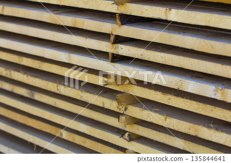 Close-up of neatly piled stack of natural brown rough wooden boards. Industrial timber for carpentry, building, repairing and furniture. Close-up of neatly piled stack of natural brown rough wooden boards. Industrial timber for carpentry, building, repairing and furniture. 135844641