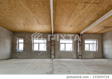 Unfinished apartment or house big loft room under reconstruction. Plywood ceiling, plastered walls, window openings, cement floor. Construction and renovation concept. Unfinished apartment or house big loft room under reconstruction. Plywood ceiling, plastered walls, window openings, cement floor. Construction and renovation concept. 135844728