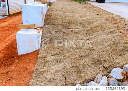 Workers lay down grass on ground next to driveway to create new lawn area for landscaping. Workers lay down grass on ground next to driveway to create new lawn area for landscaping. 135844895