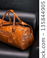 Premium tan leather duffel bag on a black leather sofa in a modern minimalist interior 135844905