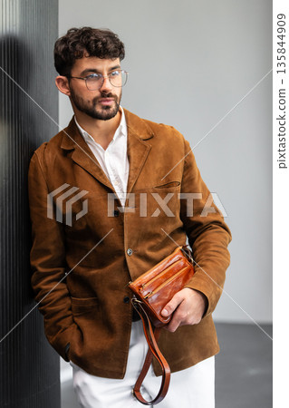 Close up of a stylish man in a brown suede jacket holding a tan leather wristlet clutch bag 135844909