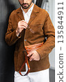 Close up of a stylish man in a brown suede jacket holding a tan leather wristlet clutch bag 135844911