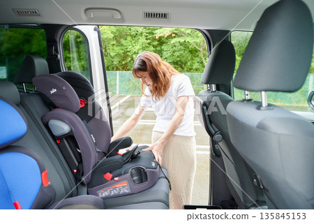 Pregnant woman installing a child seat Pregnant woman installing a child seat 135845153