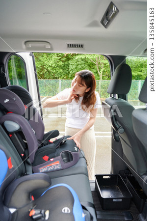 Pregnant woman installing a child seat Pregnant woman installing a child seat 135845163