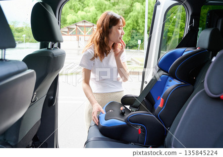 Pregnant woman installing a child seat Pregnant woman installing a child seat 135845224