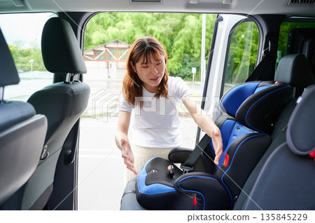 Pregnant woman installing a child seat Pregnant woman installing a child seat 135845229