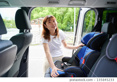 Pregnant woman installing a child seat 135845233