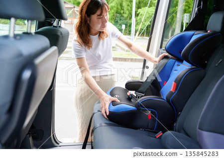 Pregnant woman installing a child seat 135845283