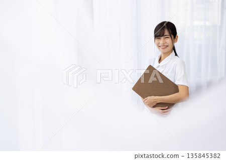 A young woman in a white coat smiling and holding a binder 135845382