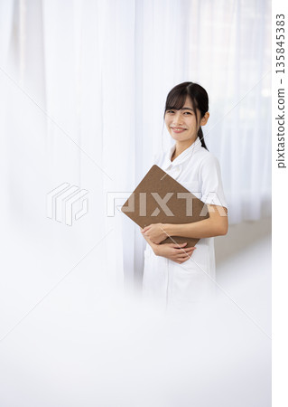 A young woman in a white coat smiling and holding a binder 135845383