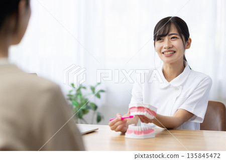 A young woman in a white coat teaching how to brush her teeth using a tooth model and toothbrush 135845472