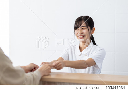 A woman in a white coat receiving a card at the reception 135845684